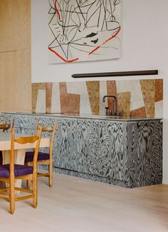 a dining room table with purple chairs next to a painting on the wall