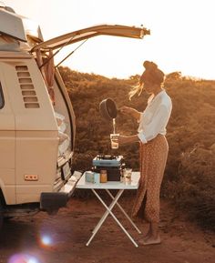 a woman standing next to a van cooking food on top of a grilling pan