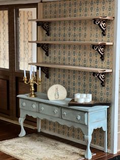 a dollhouse room with a table and shelves on the wall next to a candle holder