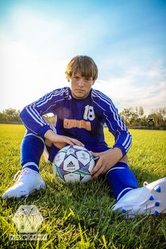 a young man sitting in the grass holding a soccer ball