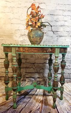 a green table with flowers in a vase on top and wood flooring underneath it