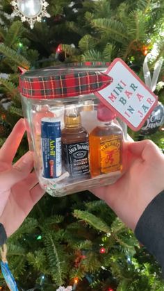 someone holding up a jar filled with different types of items in front of a christmas tree