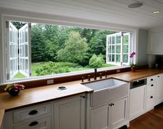 a kitchen with white cabinets and wooden counter tops next to a large window that looks out onto the yard