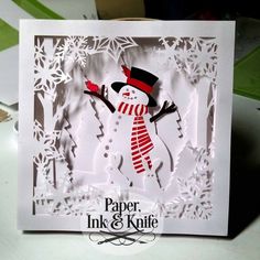 a card with a snowman cut out of paper on top of a white table