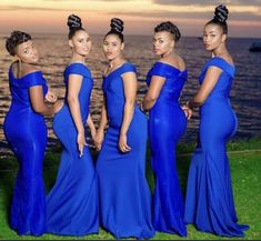 four women in blue dresses standing next to each other on the grass by the water