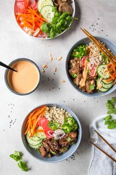 three bowls filled with meat and vegetables next to dipping sauce