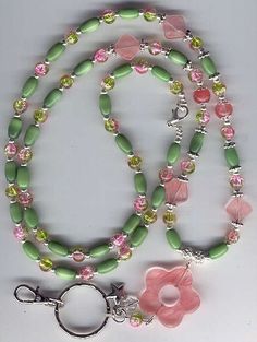 a green and pink beaded necklace with flower charm on a white table next to a pair of scissors