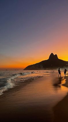 three people walking on the beach at sunset with mountains in the backgrouund