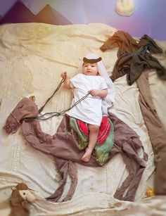 a baby laying on top of a bed next to a brown horse and some clothes