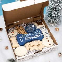 a box filled with cookies and frosting on top of a snow covered ground next to a christmas tree