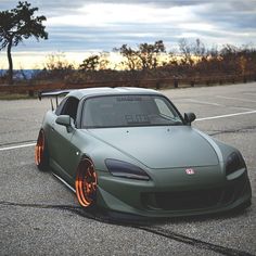 a green sports car with orange rims parked in a parking lot next to trees