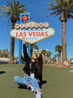 a woman sitting on the ground in front of a welcome to las vegas sign