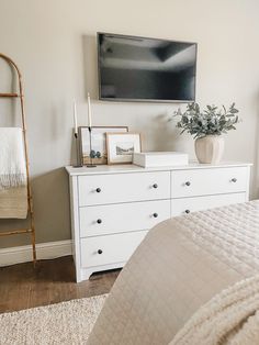 a bedroom with white furniture and a flat screen tv mounted on the wall above it