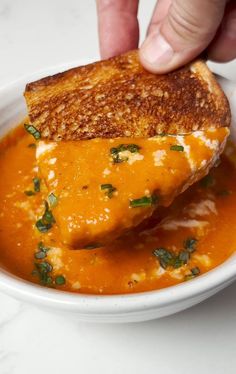 a person dipping cheese into a bowl of tomato soup with parsley on the side