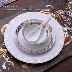 a white and gold dinner set on a place mat with spoons in the middle