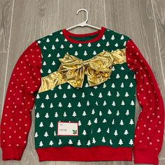 a green and red christmas sweater with gold bow on the front, sitting on a wooden floor