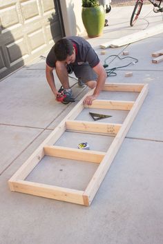 a man kneeling down on the ground working on some kind of wooden frame that is being built