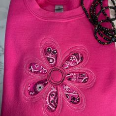 a pink shirt with an embroidered flower on the front, and a black beaded necklace hanging from it