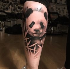 a black and white panda bear tattoo on the right leg, with triangles around it