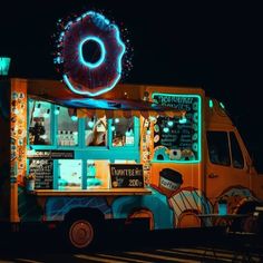 an ice cream truck with donuts on the side and lights in the background at night