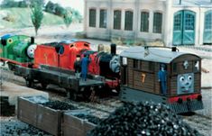 thomas the tank engine is pulling his train cars down the tracks in front of a building