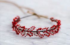 a headband with red beads and leaves on it sitting on a white wooden surface