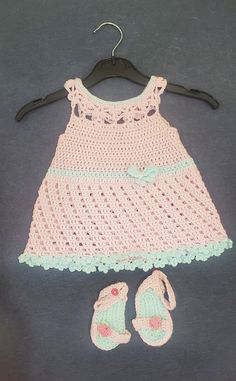 a crocheted baby dress and sandals on a hanger next to a pair of shoes