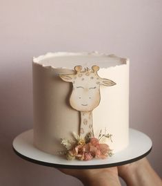 a hand holding a white cake with a giraffe on it's side