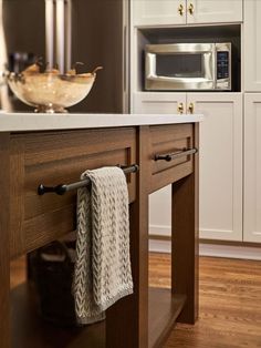 a kitchen island with two towels hanging from it's pull - out rack and a microwave in the background