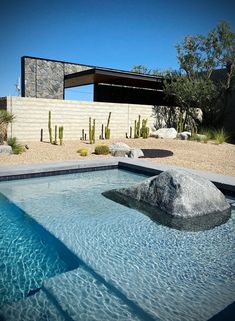 a large rock sitting in the middle of a swimming pool next to a desert style house