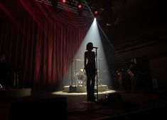 a woman standing in front of a microphone on top of a stage next to a red curtain