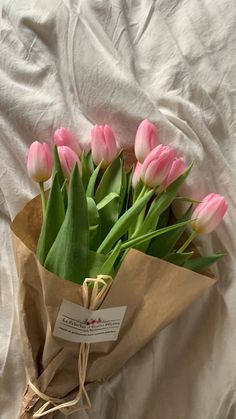 a bouquet of pink tulips in a brown paper bag on a white sheet