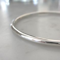 "This handmade heirloom quality sterling silver bangle is such a classic! Made from 3.2mm wide solid round sterling silver, it has such a pleasing weight. It is hand-formed and forged by me... the silver then gets hammered, hammered and hammered some more, creating a surface fully covered in tiny facets that provide a perfectly understated sparkle. The silver has been lovingly sanded and given a polished finish. Available in smooth (unhammered) finish as well, as can be seen in the last two pics Polished Hoop Bangle As A Gift, Hoop Bracelet With Polished Finish As A Gift, Minimalist Hallmarked Sterling Silver Bracelet, Minimalist Polished Bangle, Polished Sterling Silver Bracelet For Weddings, Round Everyday Bracelets With Polished Finish, Handmade Classic Round Sterling Silver Bracelet, Everyday Round Bangle With Polished Finish, Sterling Silver Bracelet With Shiny Finish