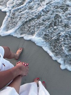 two people sitting on the beach with their feet in the sand