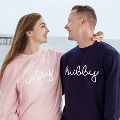 a man and woman standing next to each other near the ocean with their arms around each other