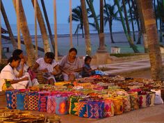 several women sitting on the ground with baskets and bags in front of them at dusk