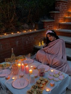 a woman sitting at a table with food and candles on it in front of her