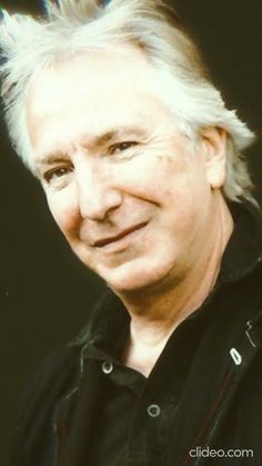 an older man with white hair and black shirt smiling at the camera in front of a dark background