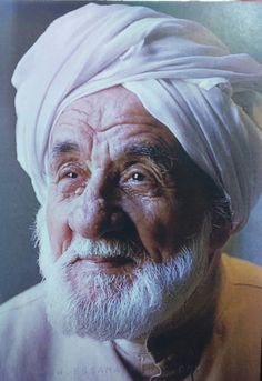 an old man with a white turban on his head looking at the camera