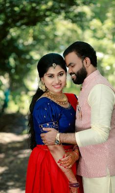 a man and woman posing for a photo in front of some trees with their arms around each other