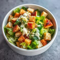 a white bowl filled with lettuce and croutons covered in ranch dressing