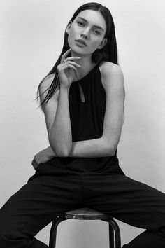 a black and white photo of a woman sitting on a stool with her hand under her chin