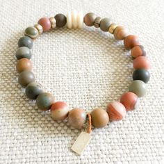 Picasso jasper raw semi-precious round stone bracelet. Colors range from neutrals to olives and grays. Features brass and bone details. Sterling silver BelleStyle logo tag. Comes in linen travel pouch. Made in USA. Earthy Jasper Beaded Bracelets With Natural Stones, Earthy Beaded Bracelets With Natural Jasper Stones, Earthy Jasper Beaded Bracelet With Natural Stones, Earthy Natural Stones Beaded Bracelets, Earthy Beige Jewelry For Everyday Wear, Earthy Everyday Beige Jewelry, Bracelet Colors, Picasso Jasper, Jasper Bracelet