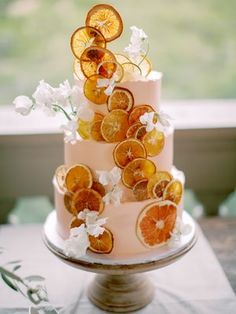 a three tiered cake with orange slices and flowers on the top is decorated with white orchids