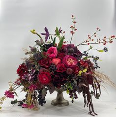 a vase filled with lots of red flowers and greenery on top of a table