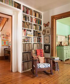 a living room filled with lots of books on top of a hard wood floored floor