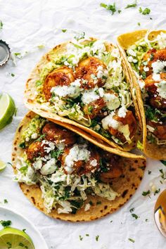 two fish tacos with limes and sour cream on top, next to a glass of beer