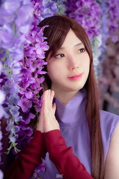 a woman with long brown hair standing next to purple flowers