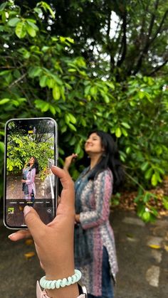 a woman taking a photo with her cell phone while standing in front of some trees