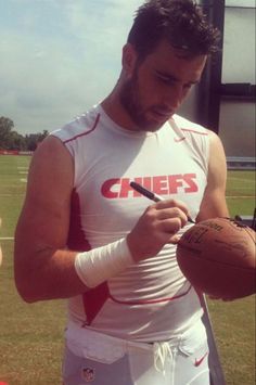 a man holding a football and writing on his cell phone while standing in the grass